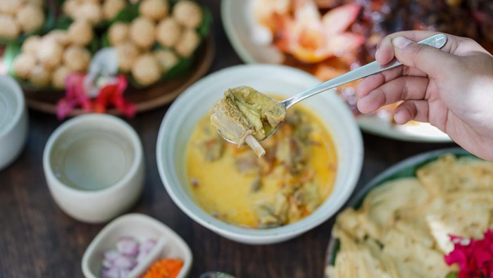 Goat curry is served in a ceramic bowl on a wooden table during a garden party.
