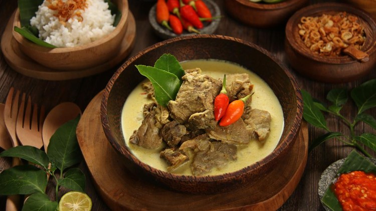 Gulai Kambing, the traditional mutton curry soup  popular in Central and East Java. Mutton chunks braised in coconut milk and curry spices. The soup is served in a shallow wooden bowl. Accompanied with red chili paste and steamed rice.