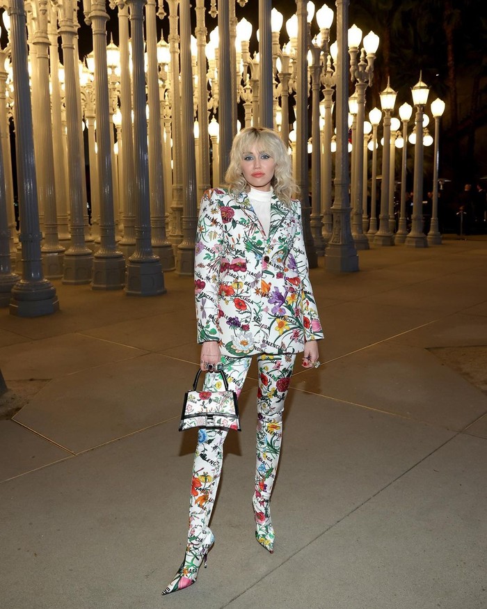 Setelan jas dengan siluet khas rancangan Demna, creative director Balenciaga, hadir dengan corak Gucci Flora, menjadi pilihan Miley Cyrus. Meski feminin, berkat padanan boots tinggi membuat secara keseluruhan gayanya menjadi lebih edgy. Foto: Instagram Gucci