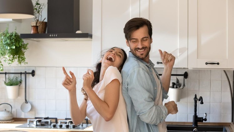 Overjoyed young family having fun in modern kitchen, dancing and laughing, happy young wife and husband moving to favorite music, enjoying leisure time, cooking dinner together, romantic date