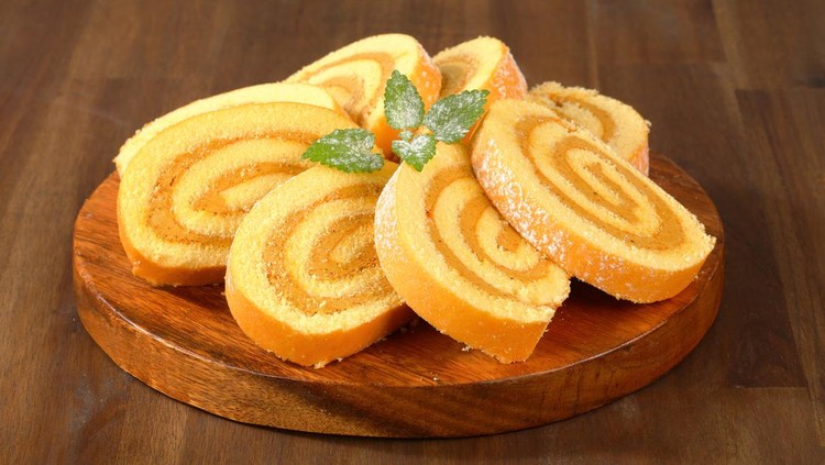 caramel swiss roll slices on a round wooden cutting board