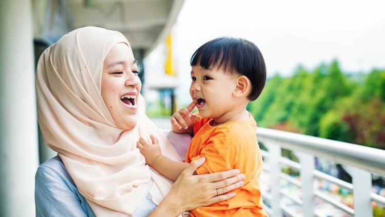 970424376 Muslim mother having fun with young son as they walk by a ledge