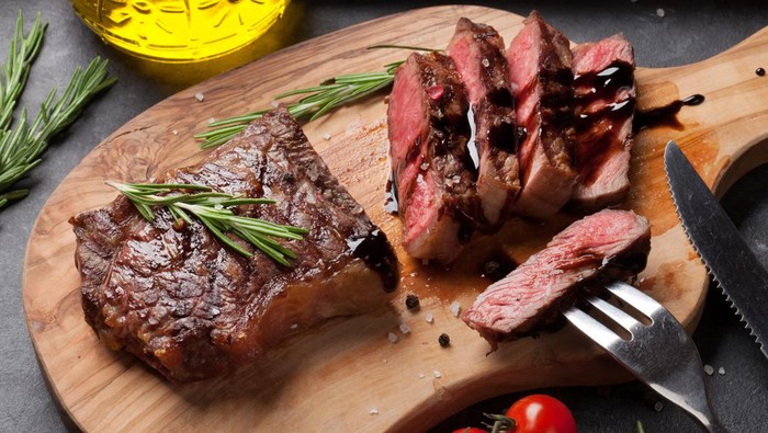 Grilled sliced beef steak on cutting board over stone table