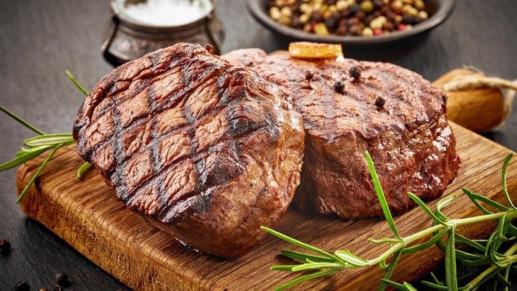grilled beef steaks with spices on wooden cutting board
