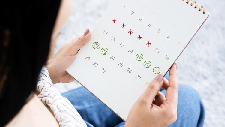 Asian woman hand holding calendar counting the date and checking her menstrual cycle planning for ovulation