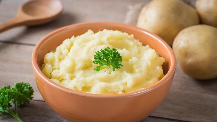 Mashed potato in bowl and fresh potatoes on wooden table
