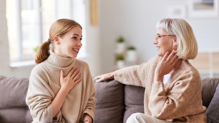mertua Young woman smiling and talking with senior mother while sitting on comfortable sofa at home together