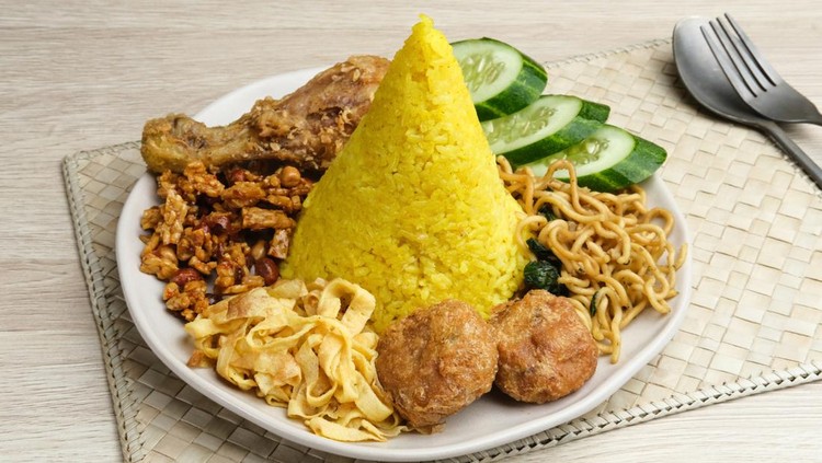 Nasi Tumpeng or Nasi Kuning is a cone-shaped rice with various side dishes. Popular to celebrate Indonesian Independence Day. Served on a plate.