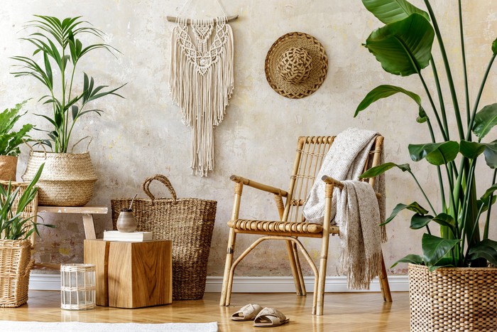 Stylish and floral composition of living room interior with rattan armchair, a lot of tropical plants in design pots, decoration and elegant personal accessories in cozy home decor. Wabi sabi concept.