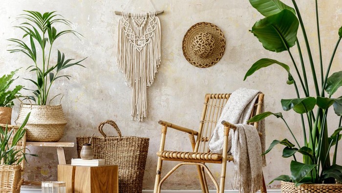 Stylish and floral composition of living room interior with rattan armchair, a lot of tropical plants in design pots, decoration and elegant personal accessories in cozy home decor. Wabi sabi concept.