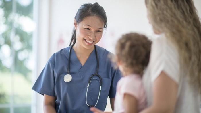 A little girl is at the doctors office for a check up. A nurse is sitting with them and talking to the mother.