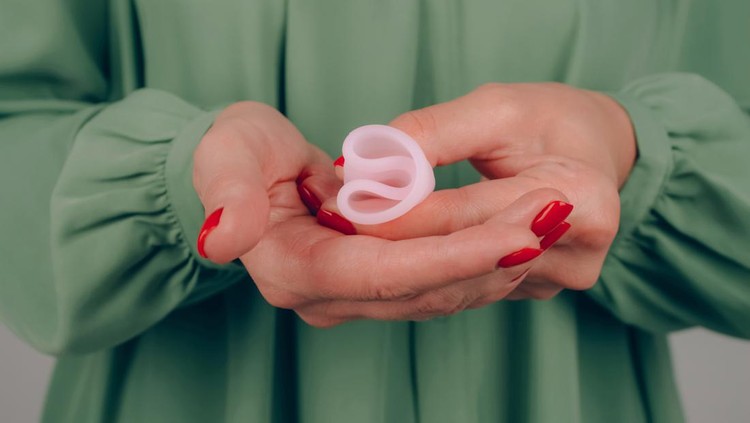 Close up of woman hands with perfect manicure, holding pink menstrual cup - demonstration of how to use, c form. Women health and hygiene concept, alternative hygiene products. Selective focus