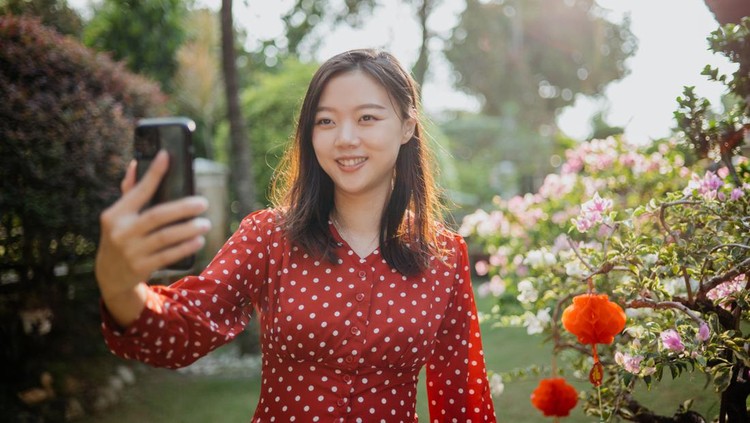 Image of an Asian Chinese woman video calling family and relatives with smartphone for online Chinese new year gathering