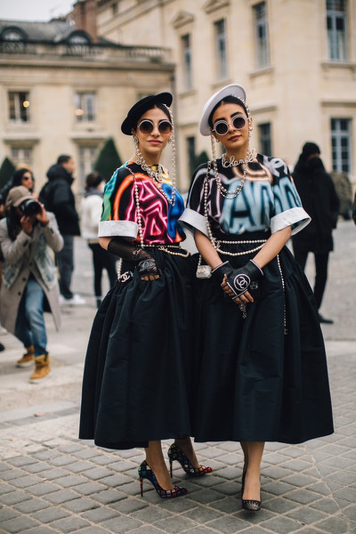 Graphic T-shirt nyentrik dipadukan dengan topi dan rok hitam bernuansa klasik diadopsi kedua undangan PFW ini. OOTD kembar mereka semakin lengkap dengan kalung, ikat pinggang, dan sarung tangan Chanel. Foto: Livingly/IMAXtree