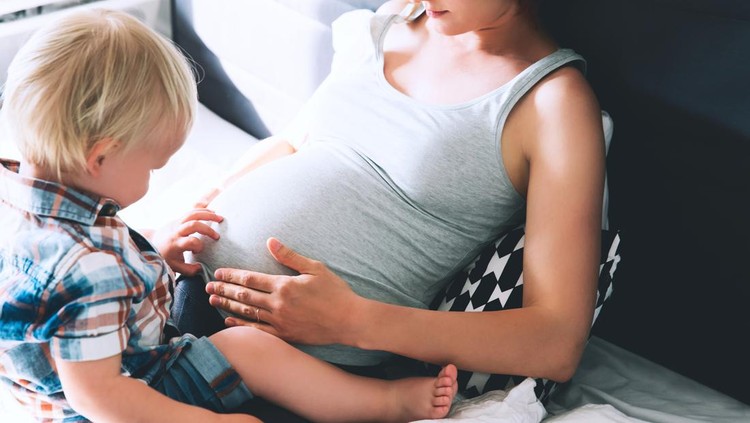 Pregnant mother and son are talking and spending time together in bed at home. Little child boy looking at her mother pregnant tummy. Pregnancy, family, parenthood, preparation and expectation concepts.