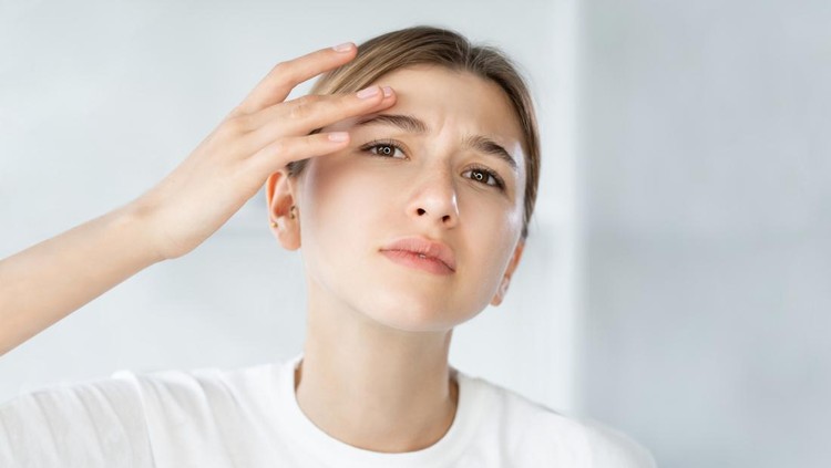 Sensitive skin. Acne problem. Zit treatment. Frustrated young woman touching itchy dry face wrinkle on white defocused background.