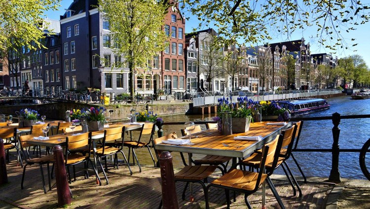 Restoran di Belanda Restaurant tables lining the beautiful canals of Amsterdam under blue skies during springtime, Netherlands