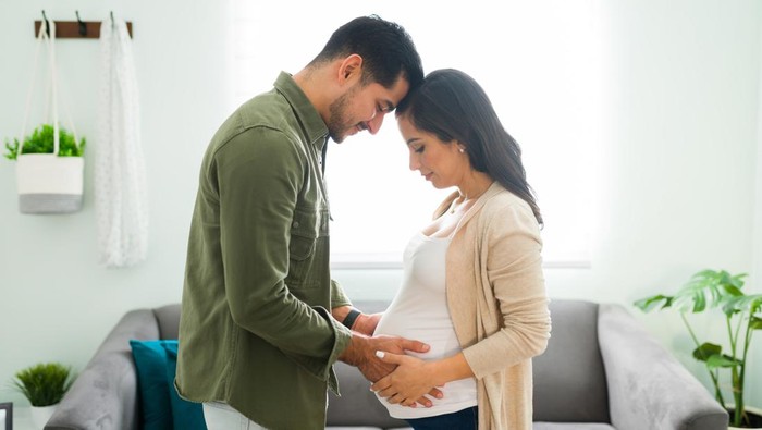 Side view of a future mom and dad holding hands with their heads together. Beautiful beaming couple looking and gazing at the pregnant woman's belly