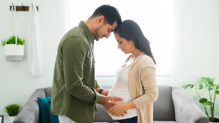 Side view of a future mom and dad holding hands with their heads together. Beautiful beaming couple looking and gazing at the pregnant woman's belly