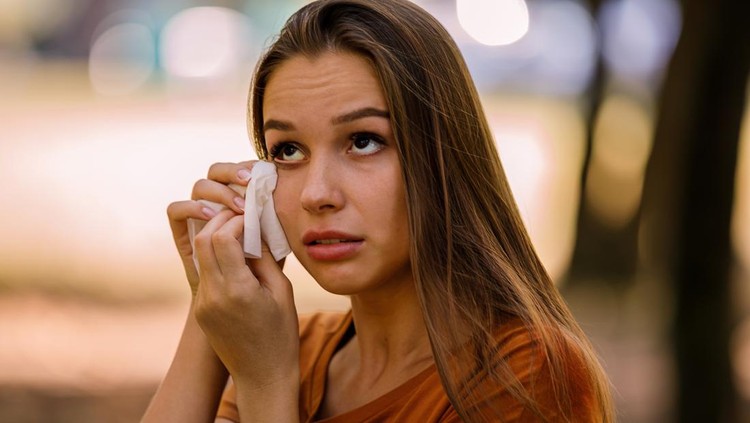 A Woman of Caucasian Ethnicity with Long Hairis Rubbing her Eyes with Paper Handkerchief Due to Problems with Sight in the Public Park.