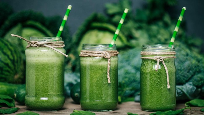 Blended green smoothie with ingredients on wooden table