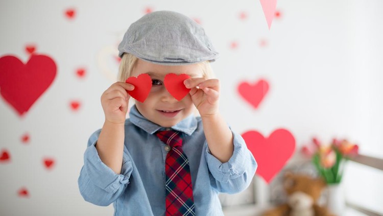 Cute blonde toddler boy, holding heart toy and playing with hearts for Valentine. be my valentine kid