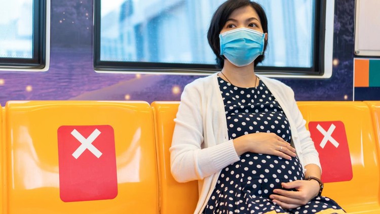 hamil vs omicron Asian Pregnant Woman in face mask touching her belly sitting on yellow seating in commuter skytrain or metro while traveling to work. Young female with social distance in pandemic virus. New normal