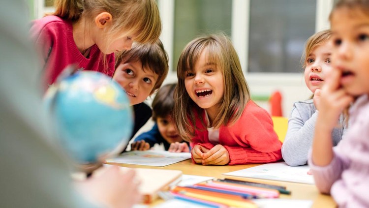 Preschool teacher teaching her children about geography. Using globe and asking the questions. Children sitting by the table and listen teacher carefully. Models in this shot are part of real kindergarten group and their teacher.