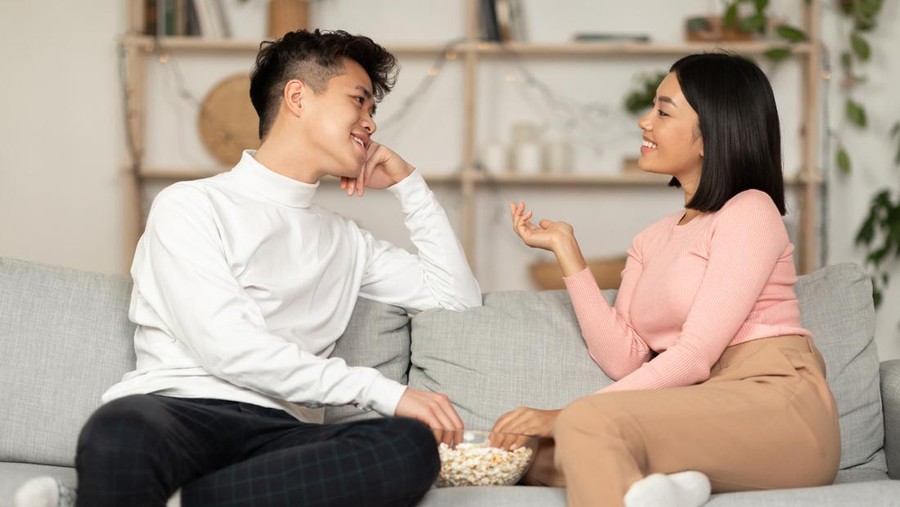 Korean Couple Flirting And Talking Enjoying Conversation During Stay-At-Home Date Spending Evening Together Sitting On Sofa Indoor. Romantic Relationship, Weekend Date Concept