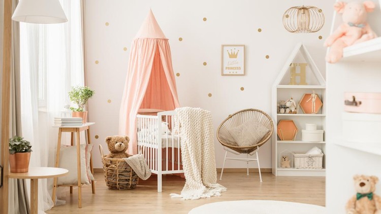 Canopied cradle between gold armchair and basket with teddy bear in pink baby's bedroom interior
