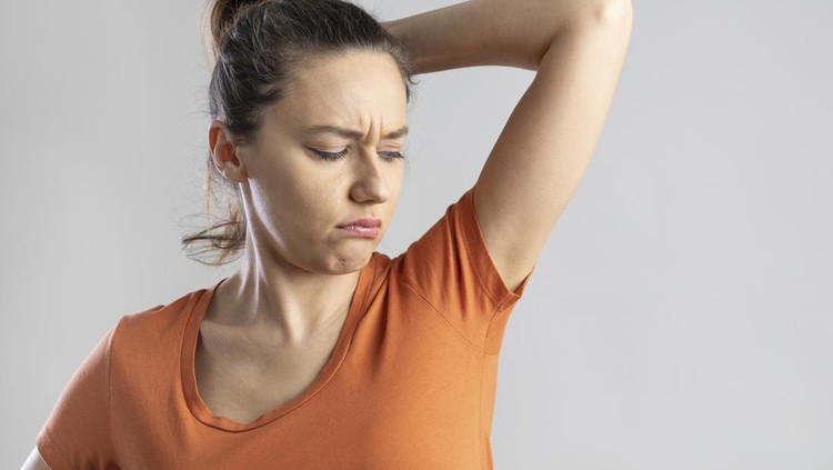 Young woman who sniffs armpits and her face is negative on isolated gray background