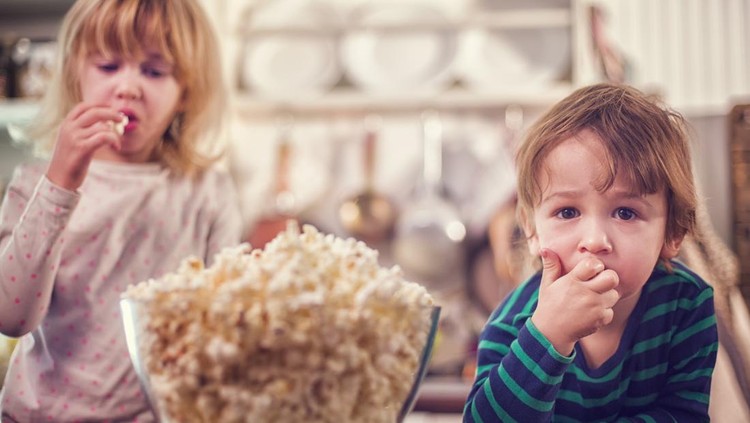 Cute little kids eating fresh homemade popcorn out of lage bowl.