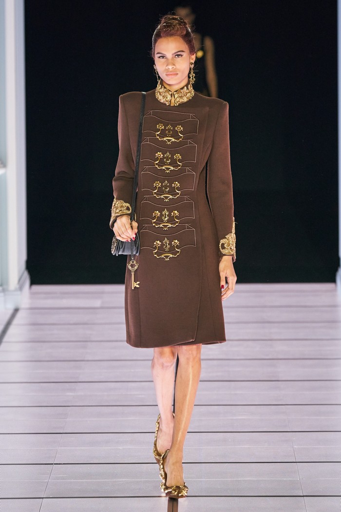 Sebuah dress coklat berhias ornamen emas pada bagian kerah juga menunjukan rupa perabotan. Bordiran bentuk laci meja lengkap gagang laci tersusun tepat di tengah gaun. Foto: vogue.com