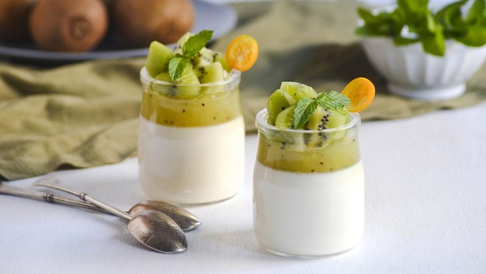Italian dessert panna cotta in glass jars with kiwi fruit jelly decorated with pieces of fresh kiwi and mint leaf on white background. Copy space