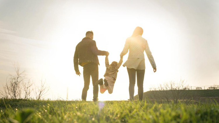 Happy parents playing with their daughter in the park. Space for copy. From behind.