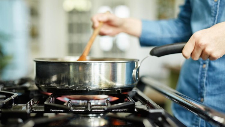 Close-up midsection image of woman cooking food in frying pan. Utensil is placed on gas stove. Female is stirring food in cooking pan. She is preparing food in domestic kitchen.
