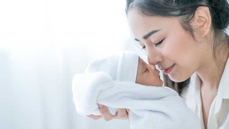 bayi baru lahir Close up shot of Asian mother kiss her newborn baby in front of white curtain in bedroom.