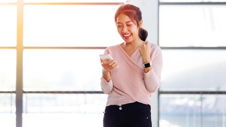 Ilustrasi wanita tertawa Young Asian girl looking at her mobile phone and get excited inside the building. One beautiful woman is happy watching at smartphone indoors.