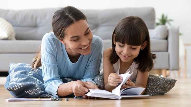 Ilustrasi ibu dan anak membaca buku Caring smiling mother reading book with little kid girl lying on warm floor at home, mom or baby sitter playing having fun telling fairy tale to child daughter, underfloor heating, family activities