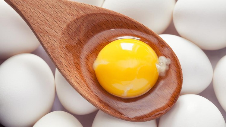 Egg yolk in wooden spoon on eggs. Close up.