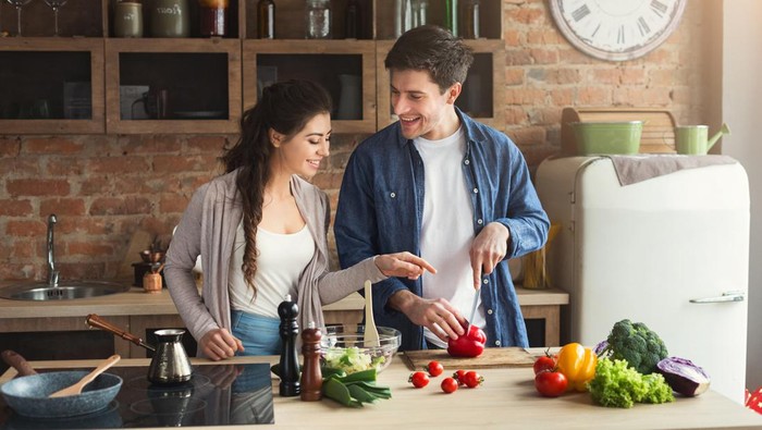 Happy couple cooking dinner together in their loft kitchen at home. Man preparing vegetable salad for his girlfriend, copy space