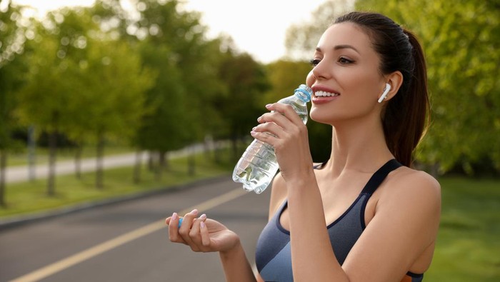 Beautiful woman in fitness clothes drinking water outdoors