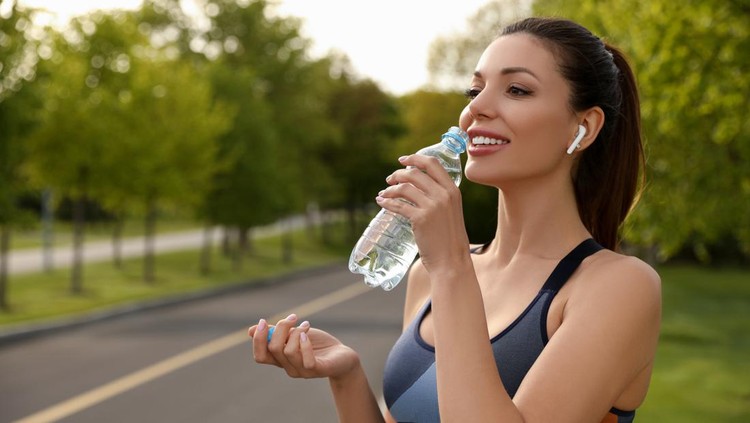 Beautiful woman in fitness clothes drinking water outdoors