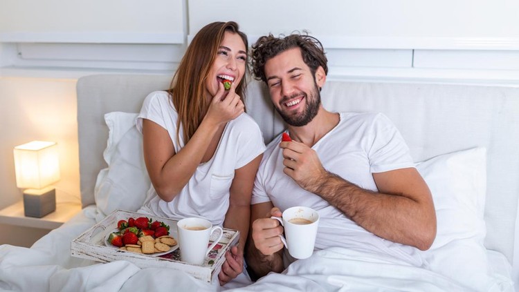 Young married couple in love eating breakfast in their bed. Good morning! Healthy breakfast in bed. Young beautiful love couple is having breakfast in bed.