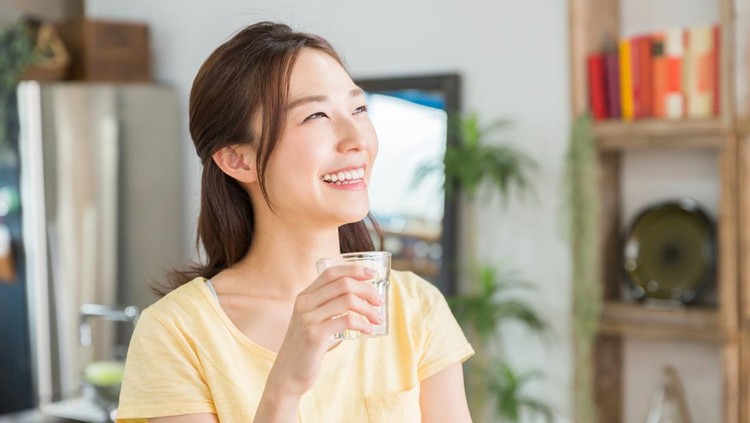 young attractive asian woman who drinks water in a kitchen