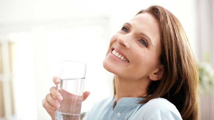 Ilustrasi Minum Air Mineral A mature woman looking away happily as she holds a glass of water