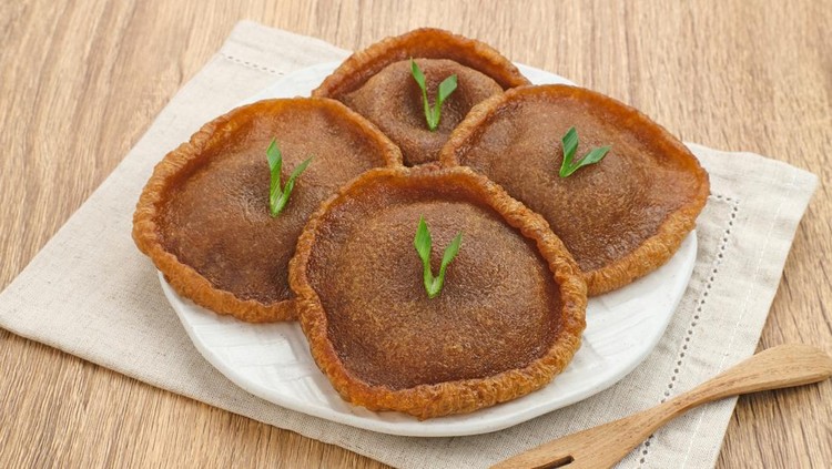 Kue Cucur is Indonesian traditional snack, made from rice flour and palm sugar and then fried. Served on white plate on wooden background. Selected focus.