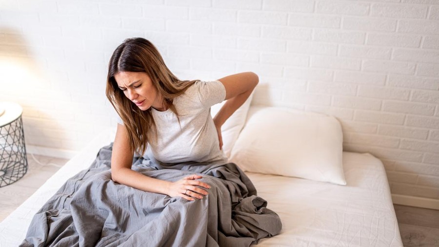 Mid adult woman having back pain after waking up in bed in the morning.