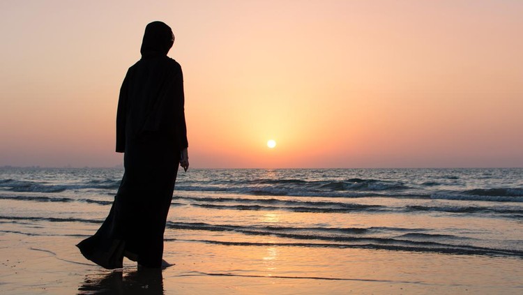 Woman in hijab standing on the beach looking at horizon