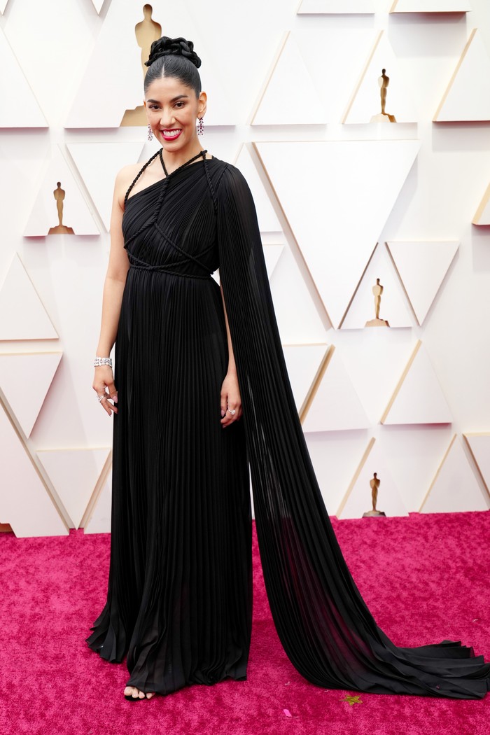 Stephanie Beatriz yang namanya kian populer sejak bermain di Brooklyn Nine Nine dan juga kini jadi pengisi suara di Encanto, mengenakan gaun one shoulder hitam dari Dior haute couture. Detail tali dan train jadi focal points dari desain gaun ini. Foto: FilmMagic/Jeff Kravitz/courtesy of Dior